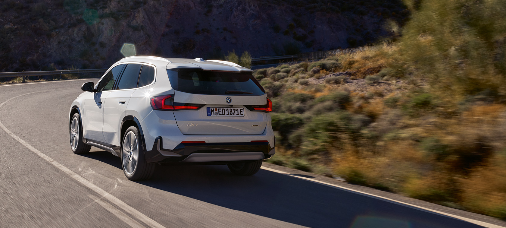 BMW iX1 U11 BEV driving dynamics highlights video BMW iX1 U11 BEV 2022 Mineral White metallic two third rear view mountain road driving driving dynamics highlights video