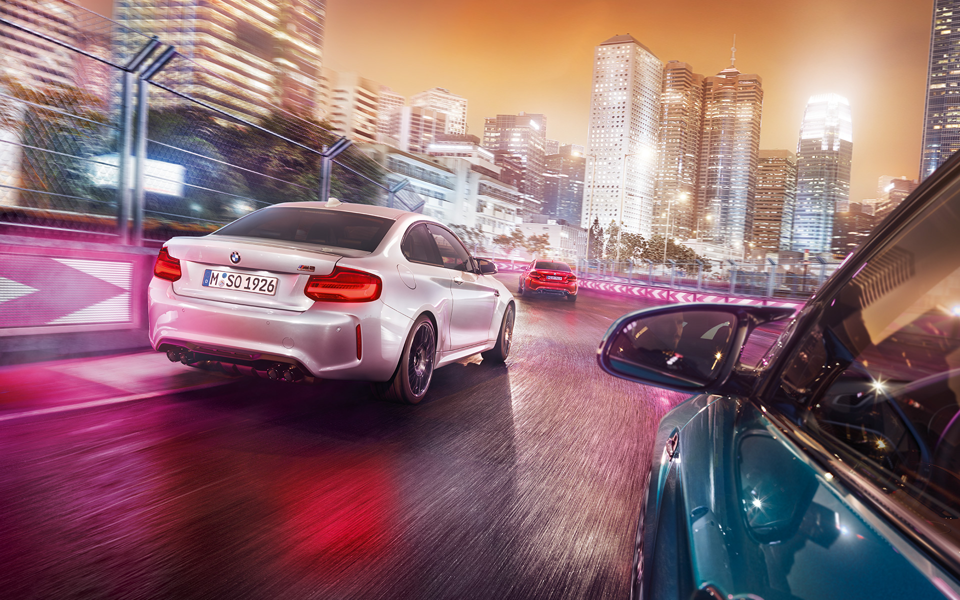 BMW M2 Competition in rear view Three BMW M2 Competition in rear view driving on race track in front of illuminated skyline.
