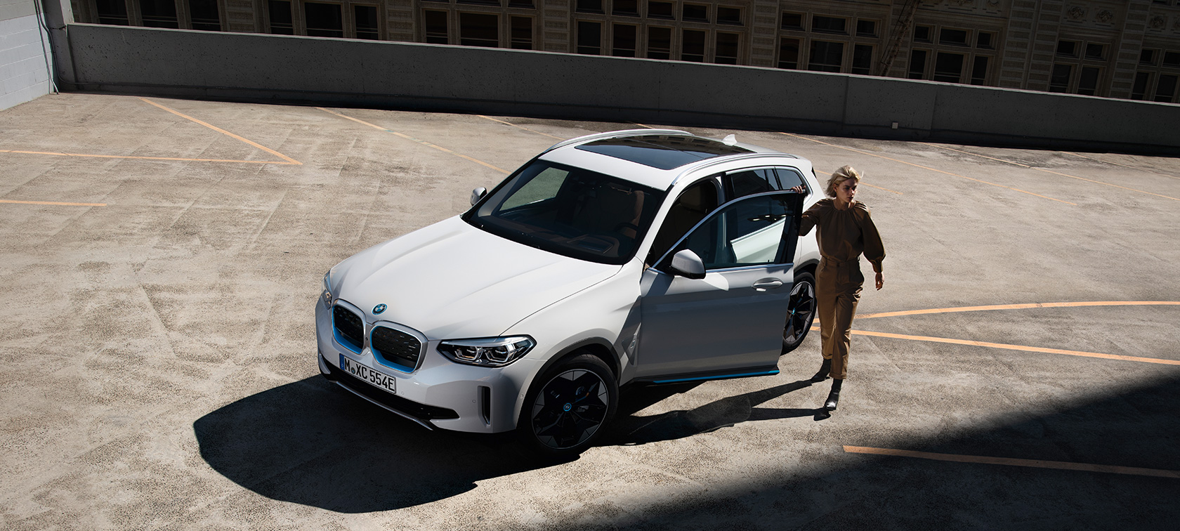 BMW iX3 G08 three-quarter front view with woman BMW iX3 G08 2020 Mineral White metallic three-quarter front view with woman in urban setting