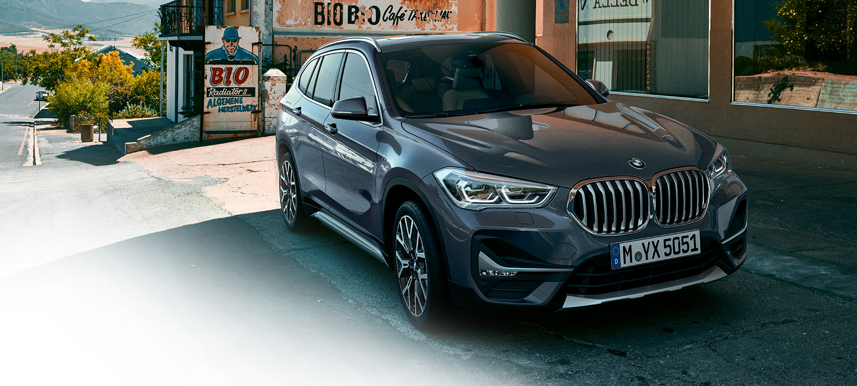 BMW X1, three-quarter front view. BMW X1, three-quarter front view standing in front of urban scenery.