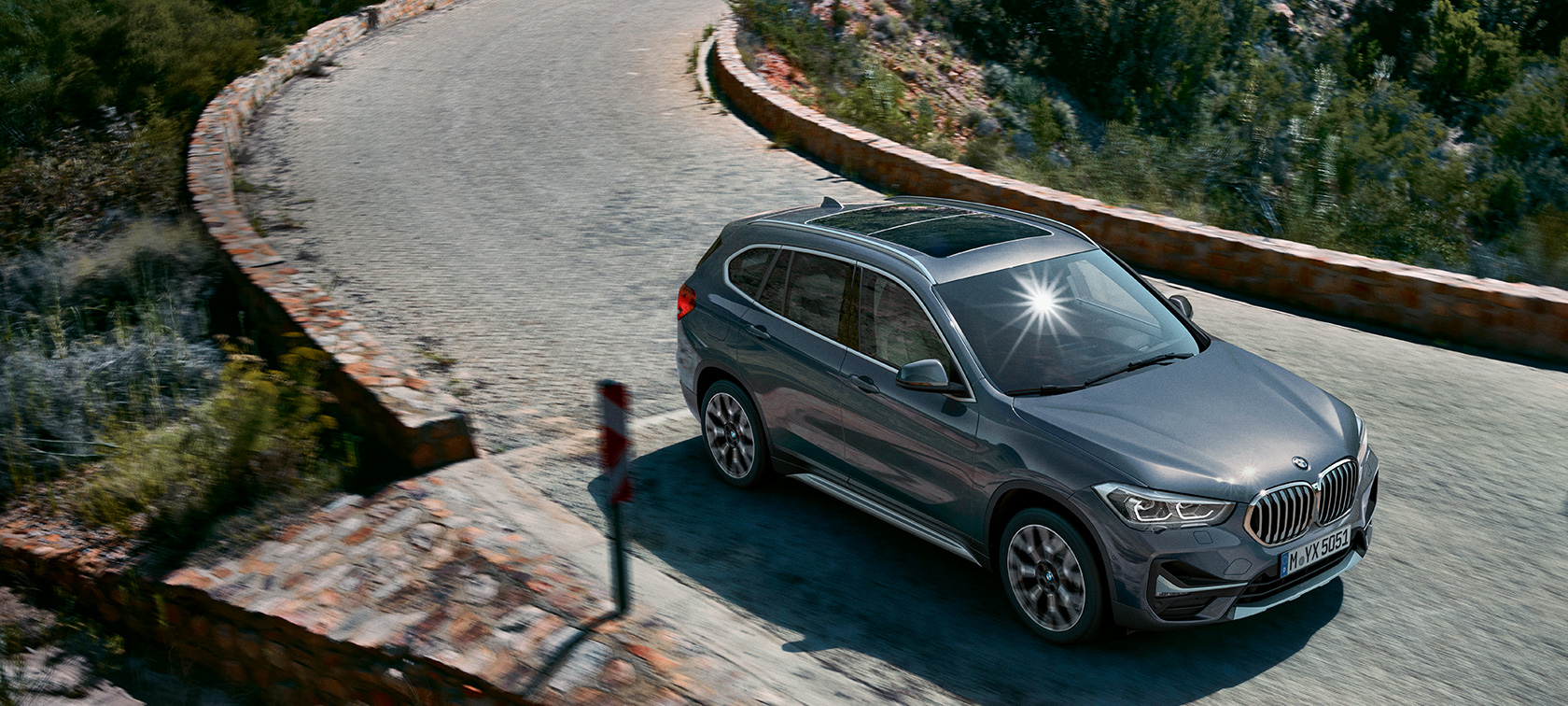 BMW X1, three-quarter front view. BMW X1, three-quarter front view driving in front of mountain scenery.