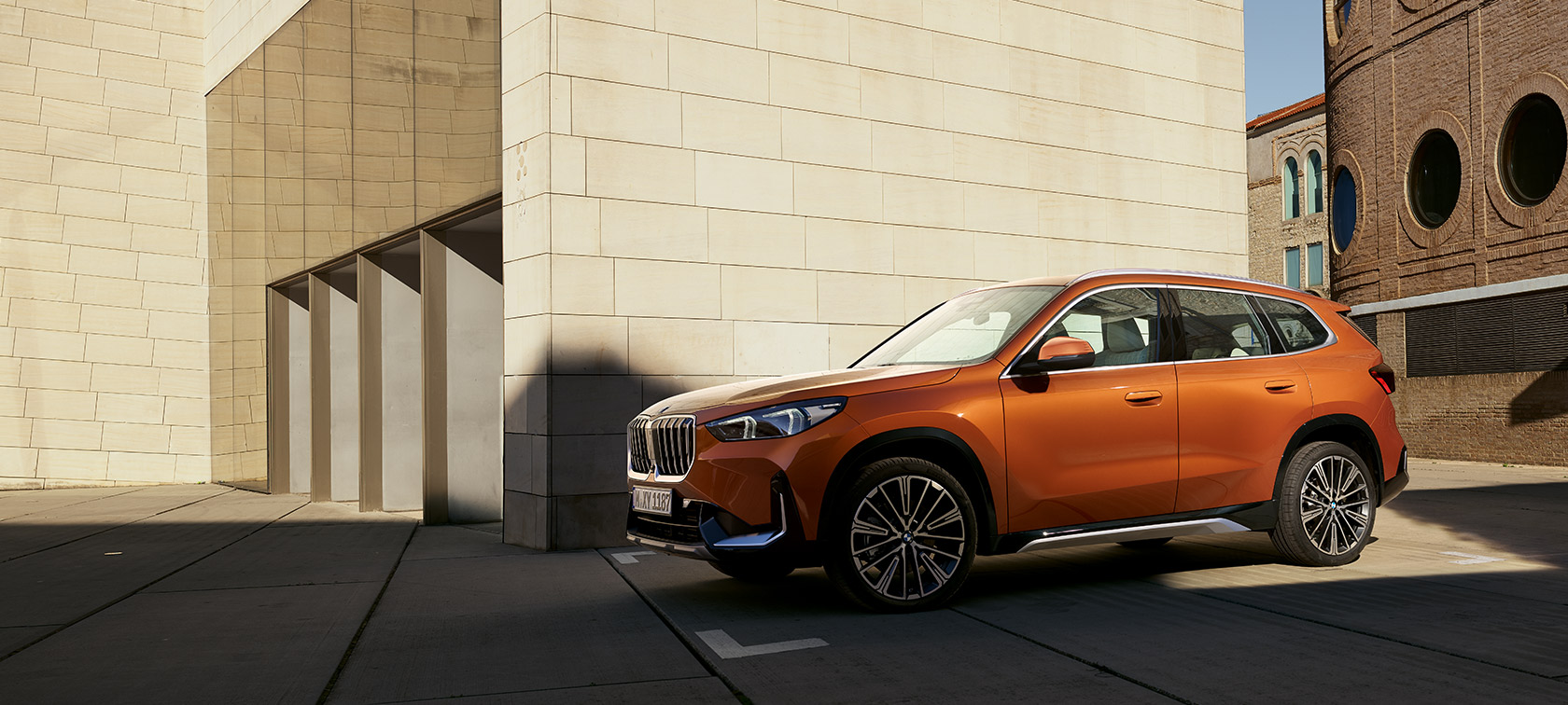 BMW U11 X1 xLine Utah orange metallic three quarter front view BMW U11 X1 xLine Utah orange metallic three quarter front view still in front of building