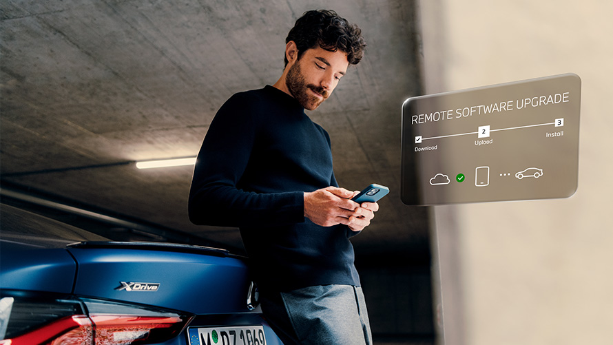 Man leans against rear of BMW and looks at his smartphone Remote Software Upgrade Remote Software Upgrade Man leans against rear of BMW and looks at his smartphone